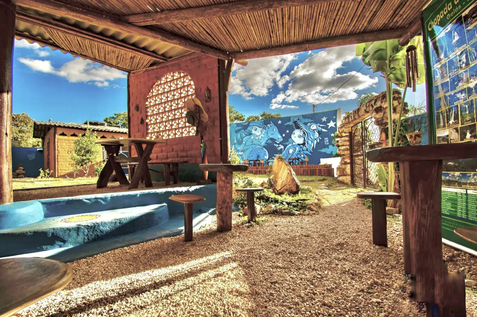 Lounge coberto em bioconstrução, com mural azul e pátio de pedra, na Shanti Pousada